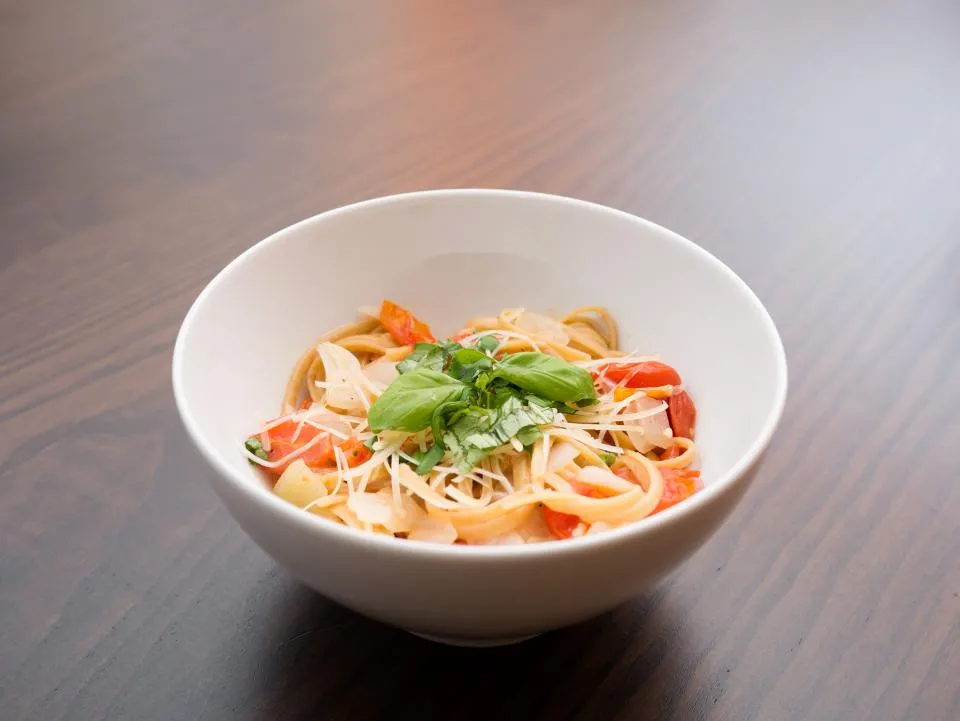 나무 식탁 위 흰 그릇에 담긴 토마토 탈리아텔레와 바질, 치즈 가루